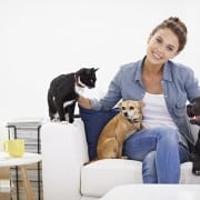 A woman sitting on a sofa with many pets near her.