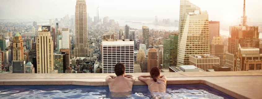 Couple in a pool overlooking the city and large buildings. Living the condo life.